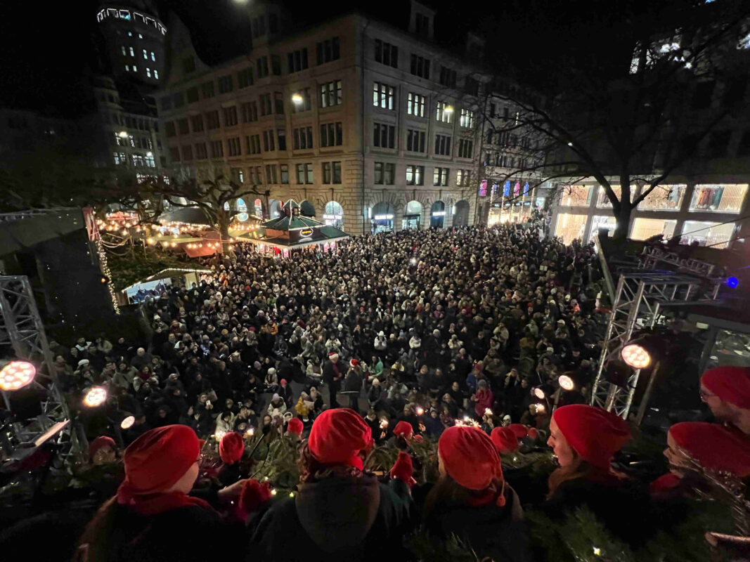 Blick der Sängerinnen und Sänger vom Singing Christmas Tree in Zürich auf den Werdmühleplatz, den Weihnachtsmarkt und das grosse Publikum.