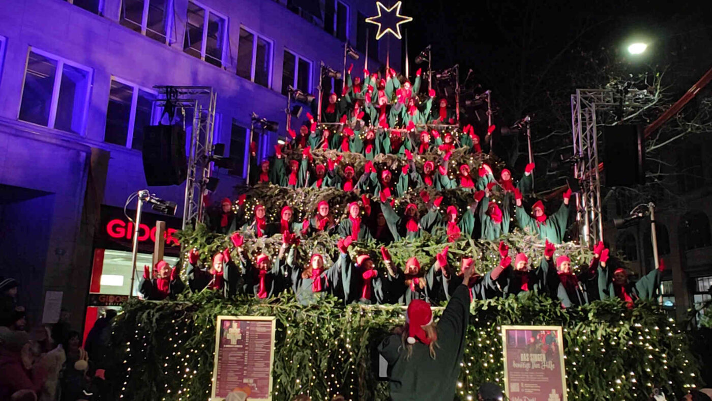 Fun Chor von Fatima Mestani singt als Weihnachtschor auf dem beleuchteten Singing Christmas Tree am Werdmühleplatz in Zürich.